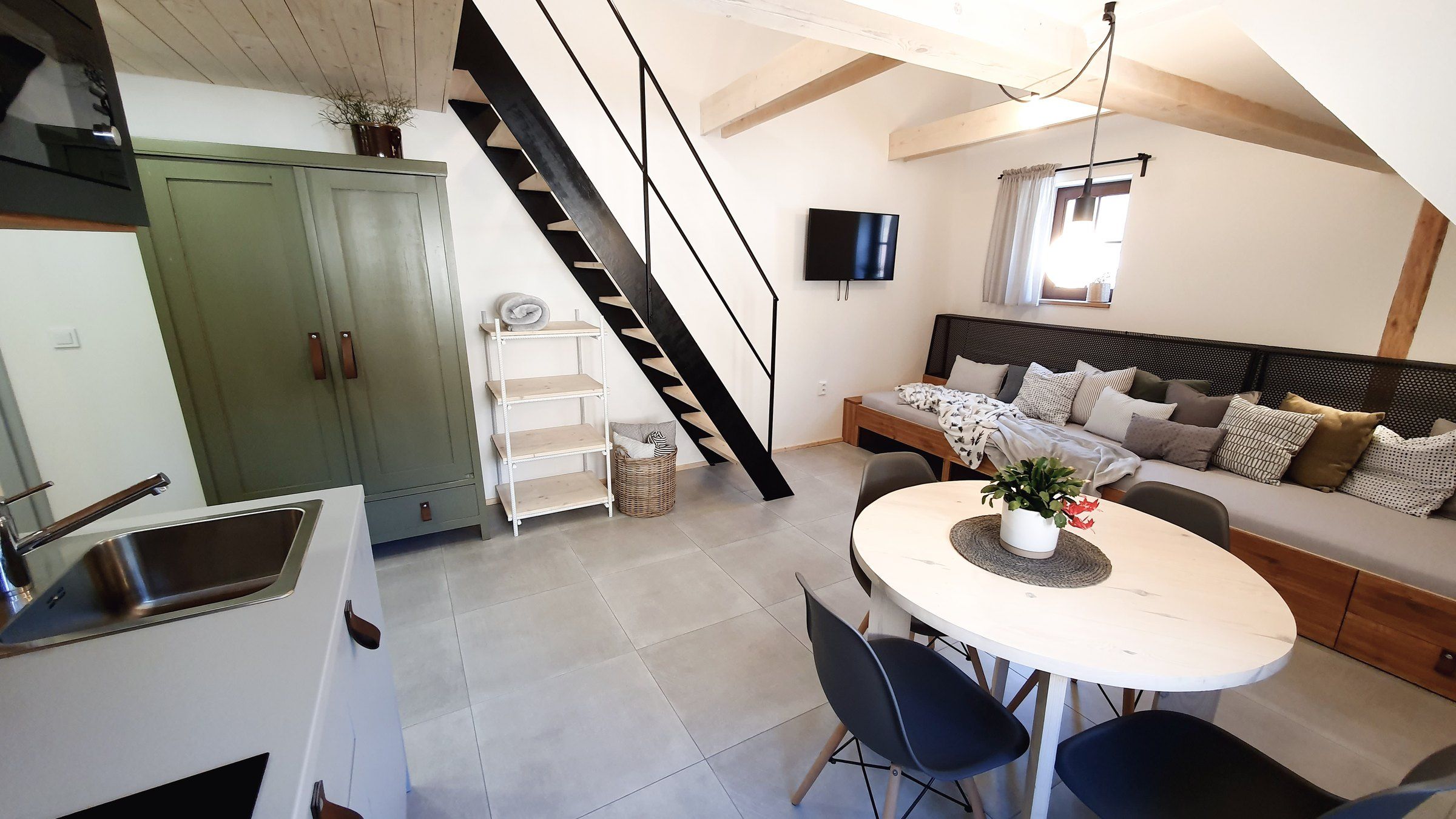Apartmán IV: zelená skříň, kuchyňský kout, schody na galerii a lůžko s polštáři u okna