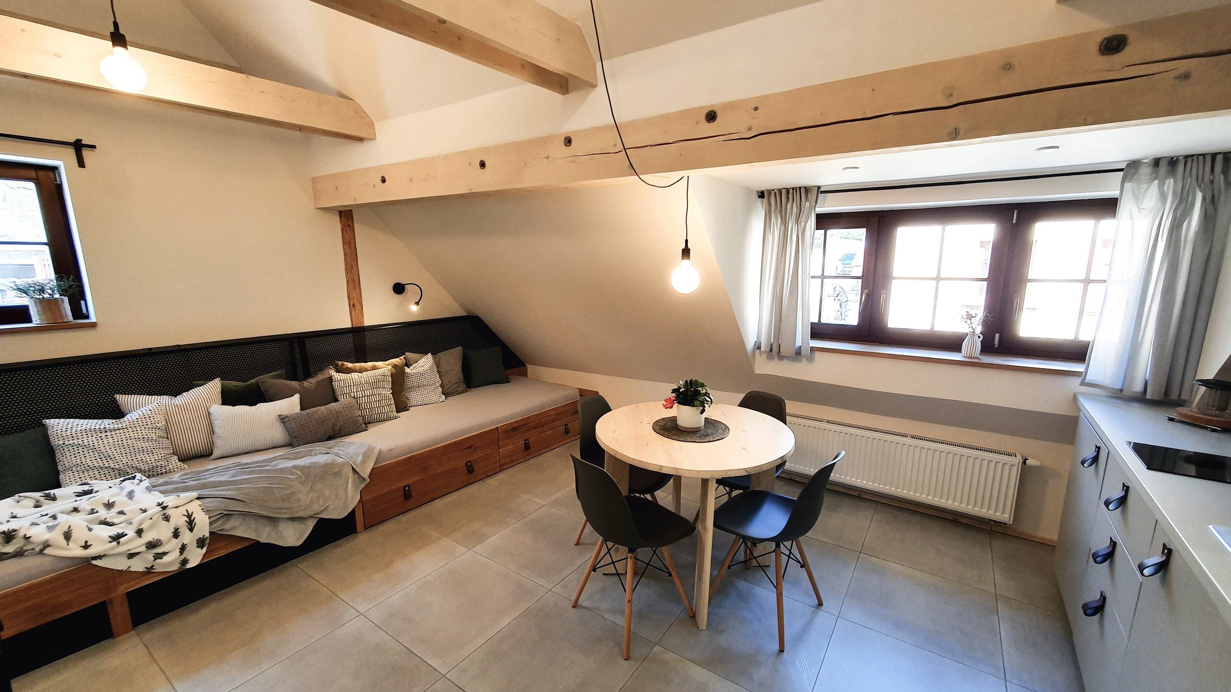 Lůžka s polštáři a stůl u okna v apartmánu IV