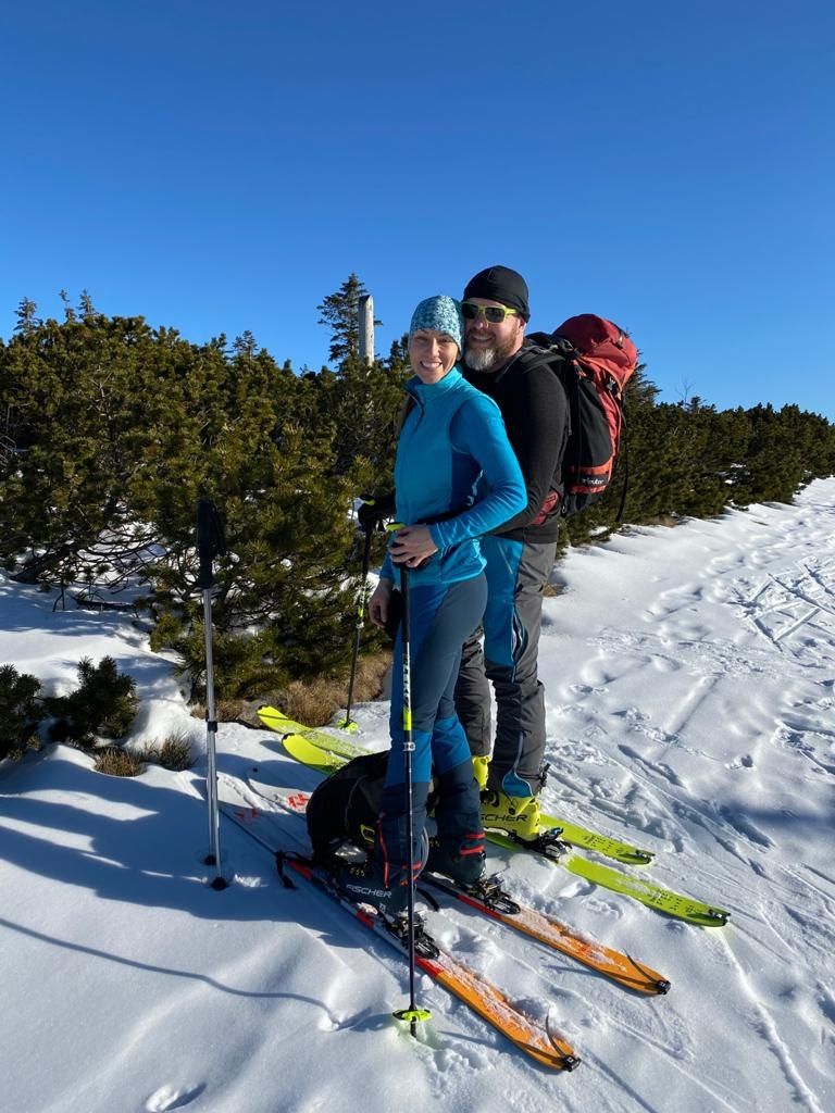 Petra a Petr na skialpech na horách, za nimi kosodřevina a modré nebe